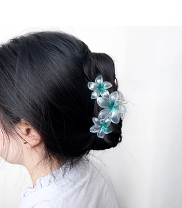 Detail of gradient blue-green plumeria hair claw clip worn on a low bun hairstyle
