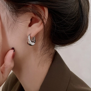 Close-up of silver C-shaped thick hoop earrings worn on ear showing sleek metallic finish