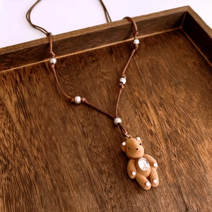 Close-up of a brown flocked bear pendant with rhinestones and pearls on a woven rope