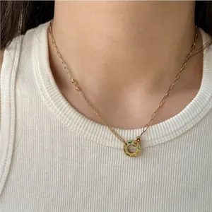 Collier doré asymétrique avec pendentif donut en émail vert sur un haut blanc