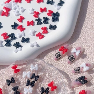 Macro detail of red, white, and black resin bow nail charms applied on press-on nails