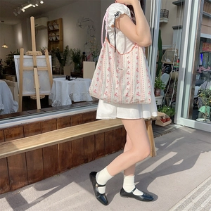 Close-up of floral canvas tote bag with pink straps and brand label in outdoor setting