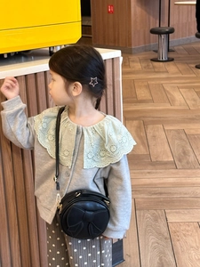Close-up of a child wearing a black round crossbody bag with a cute bow detail