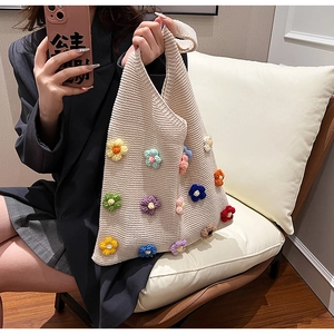 Close-up of knit tote bag featuring colorful 3D crochet flowers on a beige texture