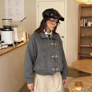 Chaqueta gris de solapa con hebillas metálicas vintage y textura de lana en una cafetería