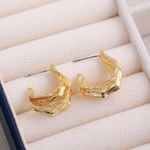 Detail of 18K gold hollow geometric wavy textured earrings on a beige velvet jewelry box
