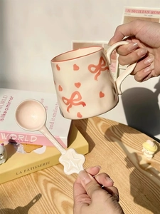Close-up of beige ceramic mug with pink bow patterns and a star-shaped spoon