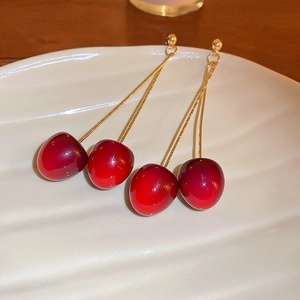 Close-up van glanzende rode kersenhanger oorbellen met elegante goudkleurige kettingen.