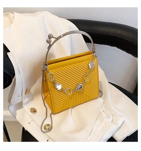 Detail of yellow quilted handbag with silver arc metal handle on white blazer jacket