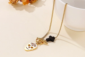 Detail of gold skull and black cross pendants with OT buckle on a link chain necklace