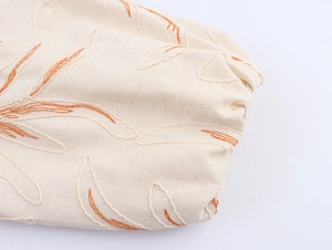 Close-up of intricate plant leaf embroidery on textured beige cotton linen jacket sleeve