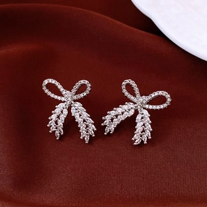 Macro view of silver bow-shaped stud earrings with zircon inlay on red silk background