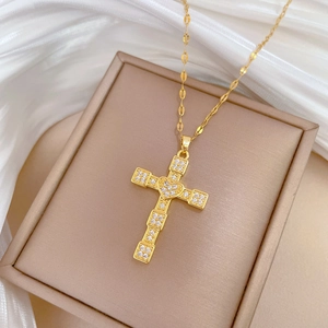 Detailed macro view of a gold cross pendant with cubic zirconia in a beige jewelry box