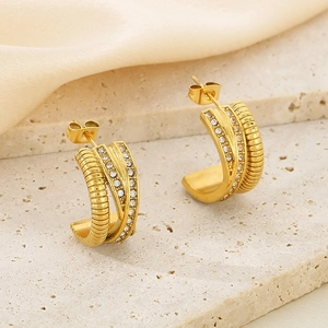 Boucles d'oreilles dorées en forme de C torsadées avec cristaux sur fond de soie