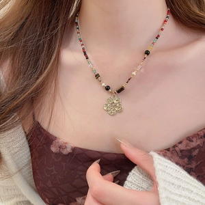 Close-up of a colorful beaded necklace with a golden clover pendant worn on the neck