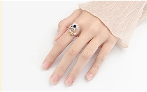 Detailed close-up of a rotating daisy and bee stress relief ring on model's finger