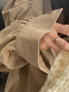 Close-up of gold ring with oval white gemstone worn by model with khaki trench coat