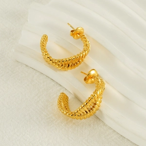 Irregular twisted rope gold titanium steel earrings on a soft textured background