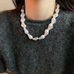 Gros plan sur un collier de perles baroques avec fermoir argenté sur un pull gris foncé