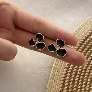 Detailed close-up of a black enamel flower stud earring with gold edge and zircon on a finger