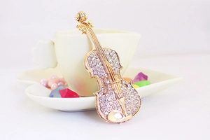Détail d'un pendentif violon doré orné de strass blancs posé contre une tasse à thé