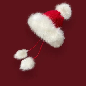 Detail of red knit Christmas hat with white plush trim and decorative pom-poms
