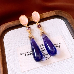 Detail of vintage gold earrings with pink, purple, and blue teardrop crystals on white fabric