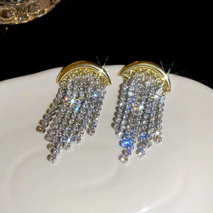 Détails de boucles d'oreilles lune dorée avec pampilles en strass sur plateau blanc