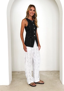 Detail of single-breasted black denim vest paired with white crochet wide-leg trousers