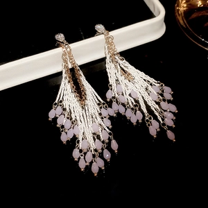 Détail de boucles d'oreilles à pompon argenté avec perles mauves et clous en cristal