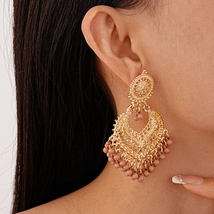 Detail of bohemian gold hollow earrings with pink beaded tassels on a model