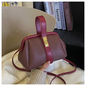 Detailed view of brown textured leather handbag with red handles and gold buckle accents