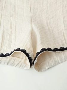Detailed macro view of beige cotton linen shorts featuring black wavy embroidery on the hem
