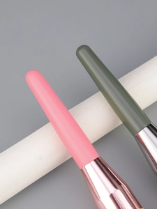Close-up of matte pink and green makeup brush handles with polished metal ferrules