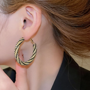 Close-up of a large black and gold twisted hoop earring worn by a model in profile view