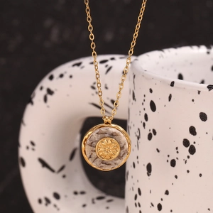 Macro shot of gold sunburst pendant with marble texture on a white ceramic mug