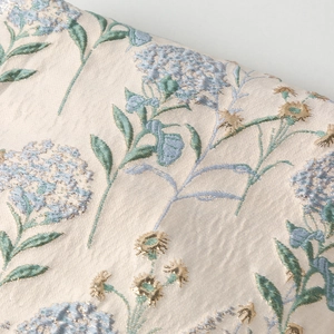 Dettaglio macro del tessuto jacquard crema con motivo di ortensie azzurre e fili d'oro