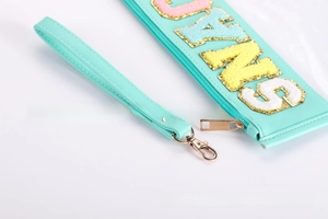 Detail of mint green waterproof PVC pouch featuring chenille letter embroidery with gold trim