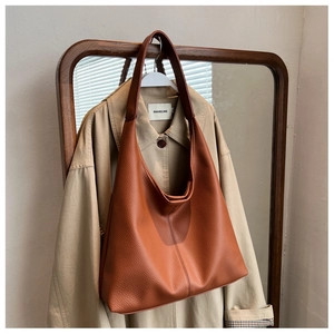 Brown PU leather tote bag with wide strap hanging on a wooden hanger against a mirror