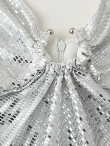 Dettaglio di abito in paillettes argento con cerniera bianca e tiralampo con logo