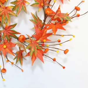 Close-up of artificial maple leaves with mini pumpkins and berries for fall decor