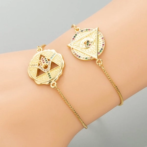 Detail of gold bracelets featuring Hamsa Hand and Evil Eye charms with colorful zircons