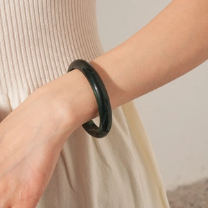 Close-up of deep green polished round bangle on wrist with knitwear texture
