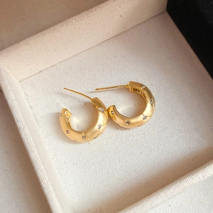 Detailed macro view of gold-plated C-shape hoop earrings with diamond-set quilted patterns