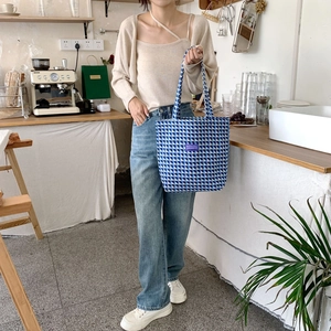 Close-up of blue and white checkered woven tote bag with purple label in a cafe setting