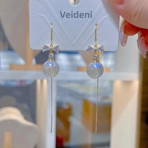 Detail of long gold tassel earrings with iridescent pearl and bow design for women