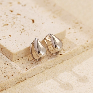 Macro shot of silver teardrop earrings on beige travertine stone with natural lighting