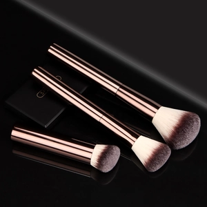 Three premium makeup brushes with rose gold handles and dual-tone bristles on black mirror