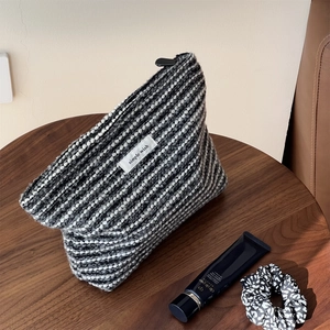 Close-up of black and white tweed cosmetic bag with woven texture and a top zipper