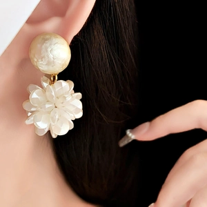 Close-up of elegant flower earrings with white shell pearl texture worn by a model